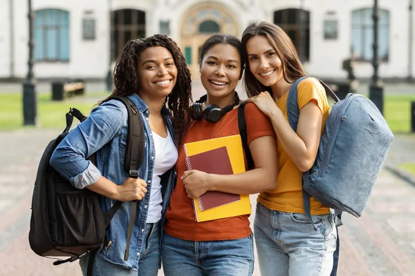 大学友谊的概念 三位多种族女学生在校园门口露面 快乐的年轻文化朋友背着背包和工作手册在相机前拥抱和微笑 — 图库照片