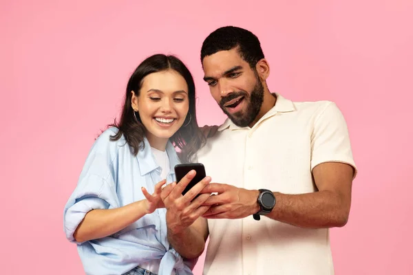 ピンクの背景に隔離された輝くスマートフォンの画面を見て 幸せなかわいい若いヒスパニック系のカップルを興奮しました 幸せな男と女のショッピング一緒にオンラインシーズン販売中 — ストック写真