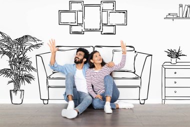 Mutlu, güzel, genç, doğulu, sakallı, gözlüklü adam ve yerde oturan uzun saçlı kadın. Oturma odasının arkası beyaz duvarla çizilmiş. Yeni eve taşınıyor, kolaj yapıyor.