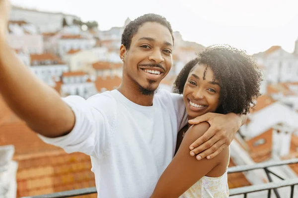 Smiling young african american guy hug lady in dress, taking selfie in city, enjoy date and travel, outdoor. Love, video call, photo for social networks, relationship, holidays, vacation and romance