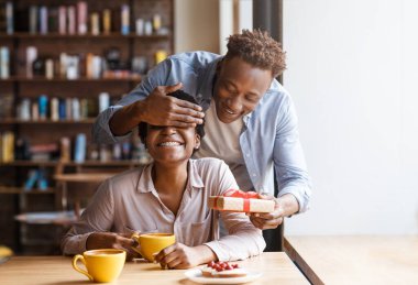 Yakışıklı genç siyahi adam restoran kafeteryasında sürpriz yapmak için kız arkadaşının gözlerini kapatıyor. Mutlu Afro-Amerikan çiftler yıldönümleri, Sevgililer Günü