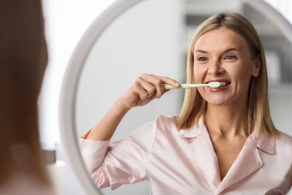 Красивая Зрелая Женщина Чистит Зубы Зубной Щеткой Рядом Зеркалом Счастливая — стоковое фото