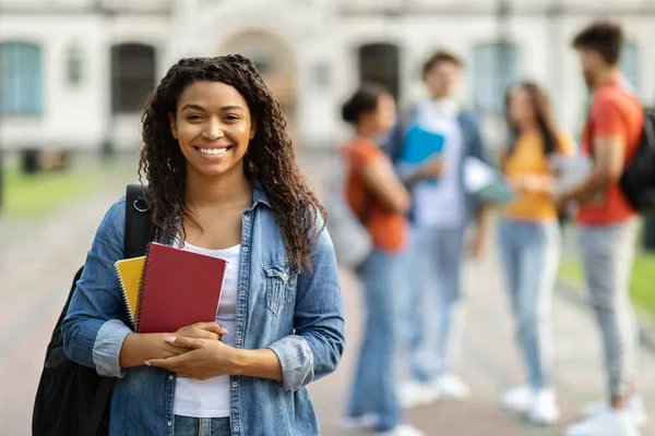 教育贷款概念 照片中快乐的黑人女学生在户外与同学和大学大楼合影时对着相机微笑 有选择性的聚焦 — 图库照片