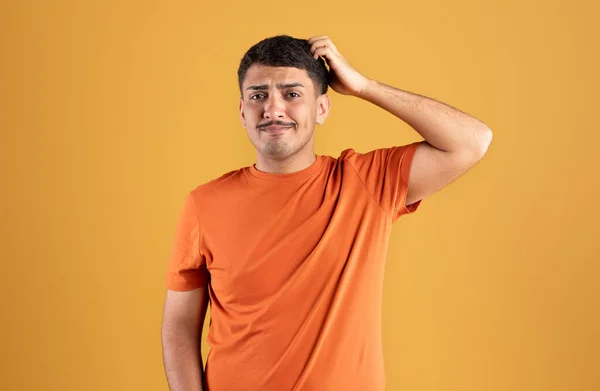 Sad pensive brazilian guy thinking and scratching head, posing isolated on orange background, studio shot. Difficult choice, ad and offer, human emotions, problem solving