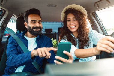 Neşeli Arap adam telefonda kadın sürücüye yol gösteriyor. Akıllı telefon kullanıyor. Araba sürerken dijital harita uygulamasına bakan çift.