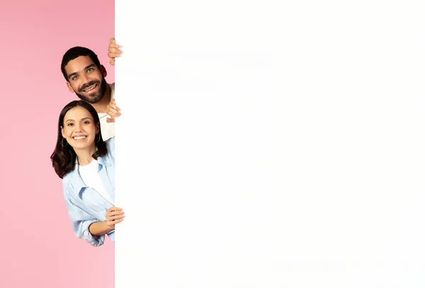 かわいい甘い陽気な若いヒスパニックなカップルは 巨大な白い空の広告プラカードと笑顔で立って ピンクの背景 モックアップ 広告のコピースペースに分離しました — ストック写真
