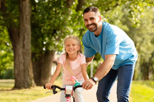 Training wheels and tender moments. Adorable girl learning to ride a bicycle with her father outdoors, dads guide to teaching biking. Daddys day out