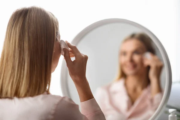 Over Shoulder View Of Mature Woman Cleansing Skin With Cotton Pad At Home, Smiling Middle Aged Female Looking In Mirror, Making Daily Skincare Routine, Removing Makeup, Selective Focus