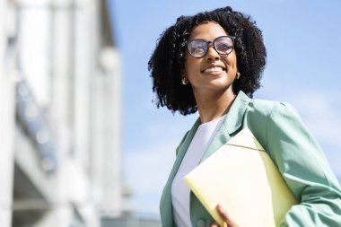 Neşeli, çekici, kıvırcık, başarılı, Afro-Amerikan iş kadını, resmi kıyafetler ve gözlük takan, yan yana yürüyen, gülümseyen, fotokopi çeken...