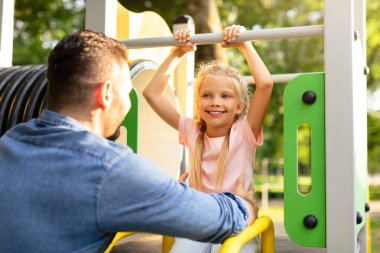 Oyun parkından hikayeler. Baba parkta küçük mutlu kızıyla oynuyor, kız kaydırağın üzerinde oturuyor ve baba çocuğa yardım ediyor. Aile Günü konsepti