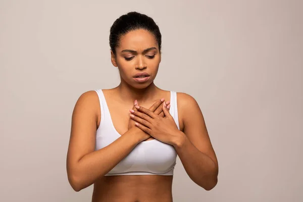 Worried unhappy young black woman suffering from acid reflux or heartburn, symptomatic indigestion or gastritis disease, isolated on gray studio background, copy space