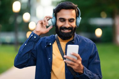 Kulaklıklı, akıllı telefonlu mutlu bir Arap, şehir içinde yürürken video görüşmesi yapıyor. Kulaklık takan, elinde cep telefonu olan, yürüyüşü seven ve şehirde en sevdiği müziği çalan mutlu bir doğulu.