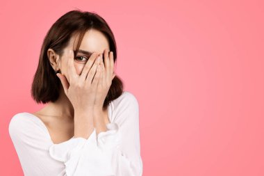 Bin yıllık beyaz tenli esmer bayanın yüzünü ellerle örttüğüne ve tek gözle baktığına sevindim. Pembe arka planda, stüdyoda izole edilmişti. Güzellik, tatil sürprizi, yaşam tarzı, reklam ve teklif, iyi haber.