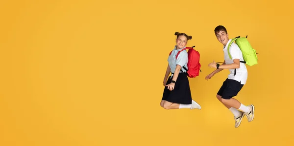 令人高兴的是 高加索少年男女背着背包跳着 空气冻结 庆祝胜利 玩得开心 在橙色工作室背景下与世隔绝 生活方式 学校教育 广告和提供服务 — 图库照片