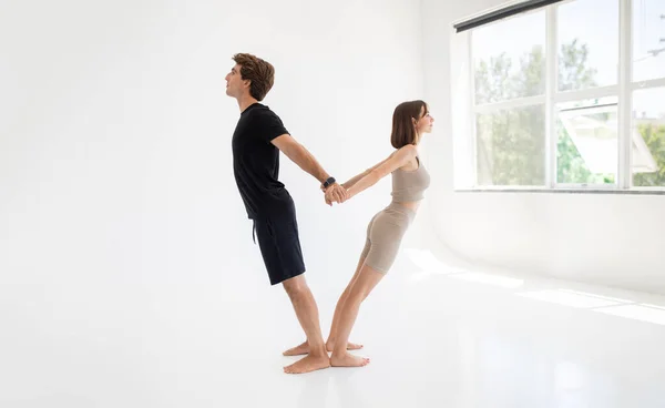 Happy calm young caucasian lady and guy in sportswear enjoy workout together, stretching body, meditate, practice yoga in gym or room interior. Teamwork, sports at home, health care