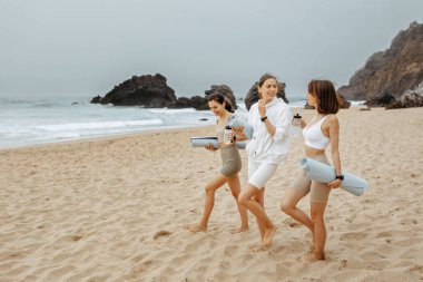 Plaj yogası Okyanus kıyısındaki egzersizlere hazırlanan genç, mutlu spor yapan kadınlar, açık havada vücut sağlığının tadını çıkarıyorlar. Yaz okyanusu pilates eğitimi