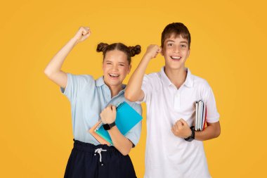 Gülümseyen Kafkas ergen kız ve erkek öğrenciler el kaldırıyor, galibiyeti ve başarıyı kutluyor, turuncu stüdyo arka planında soyutlanıyor. Eğlence, birlikte eğitim, okul eğitimi, reklam ve teklif.