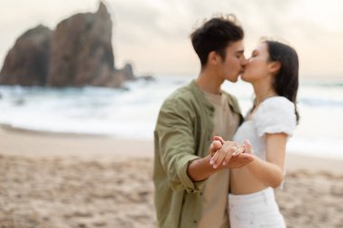 Nişanlı çift plajda romantik bir nişan günü geçiriyor, dans ediyor ve öpüşüyor, sahil şeridinde hassas anlar yaşıyor, ellere odaklanıyor, boş alana odaklanıyor.