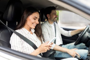 Online rezervasyon. Mutlu milenyum çifti beyaz arabanın içinde oturuyor, akıllı telefon tutan kadın, yola bakan neşeli adam, internetten oteli ayarlayan kadın, seyahat uygulaması kullanıyor.