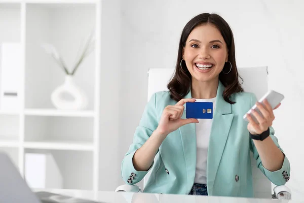 Uśmiechnięta Biała Kobieta Garniturze Pokazuje Kartę Kredytową Telefon Miejscu Pracy — Zdjęcie stockowe