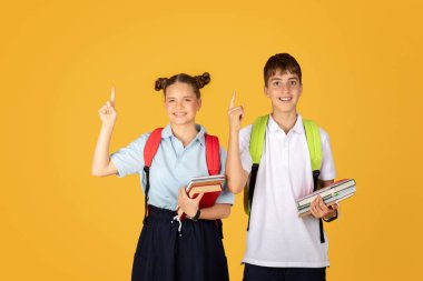 Pozitif beyaz kız ve erkek öğrenciler el kaldırıyor, parmakla işaret ediyor, fikir yürütüyor, turuncu stüdyo arka planında izole edilmiş. Birlikte okumak için bir çözüm bul, okul eğitimi