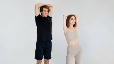 Gülümseyen beyaz erkek ve kadın spor giyimli, spor salonunda beyaz arka planda aktif bir yaşam tarzı olan, birlikte antrenman yapmaktan hoşlanıyorlar. Koçla spor, sağlık hizmetleri, ısınma hareketleri, esneme hareketleri.