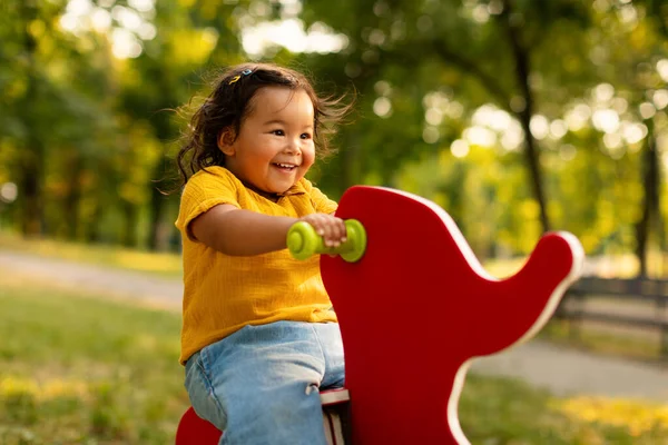 赤ちゃんの幸せと楽しい 楽しいアジアの赤ん坊のガールライディングコイルスプリング エレファント形ライダーに座って パブリックパークで屋外遊び場で楽しんで見る — ストック写真
