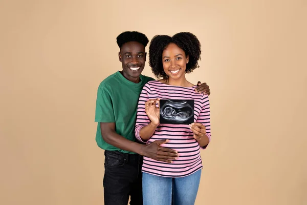 快乐的年轻黑人男人抱着大肚子的女士 享受怀孕和期待的孩子 展示超声波扫描 与米色背景 工作室隔离 父母与新生活 体格检查 — 图库照片