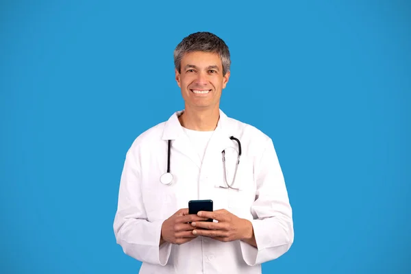 Akıllı Telefonu Tutan Mavi Arka Planda Kameraya Gülümseyen Mutlu Doktor — Stok fotoğraf