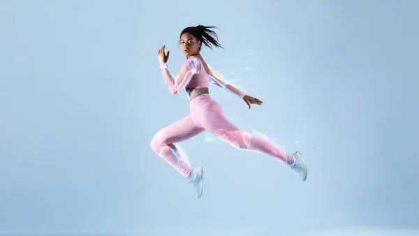 Training with modern futuristic sport technologies concept. Fit black woman in sportswear jumping or running, exercising on neon blue studio background, free space, full length. Energy and sport