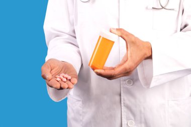 Tıbbi ilaç ve şişe gösteren profesyonel bir doktor mavi arka plandaki hastaya ilaç tedavisi öneriyor. Tanımlanamayan doktor ilaç gösteriyor.