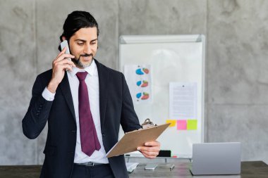 İş kavramı. Yakışıklı, orta yaşlı bir işadamı elinde kağıtlarla iş görüşmesi yapıyor. Pazarlık anlaşması yapıyor. Yönetici, bilgisayarını ofiste çalışma masasına çeviriyor. Boşluğu Kopyala