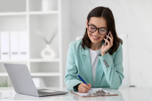 令人高兴的是 年轻的高加索女商人穿着西服 戴着眼镜 带着电脑在办公室里打电话 多重任务 商业和工作 官方生活方式和广告 专业职业 — 图库照片