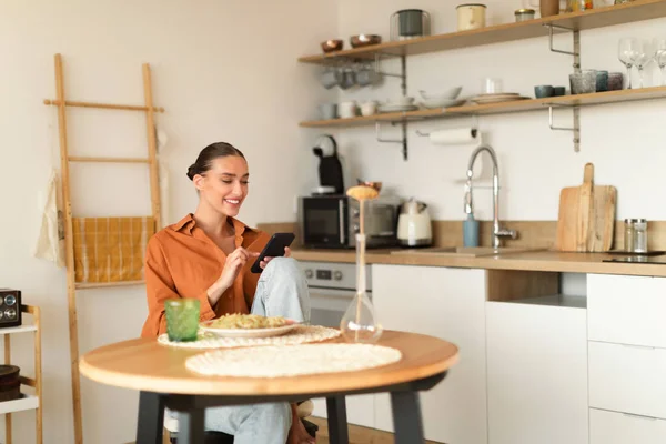 Glada Unga Kvinna Sitter Köket Använda Smartphone Medan Äter Middag — Stockfoto