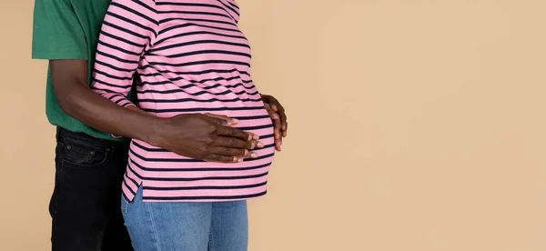 年轻的黑人男人抱着大肚子的妻子 感觉孩子的运动 享受怀孕和期待的孩子 孤立的米色背景 工作室 父母和新生儿 — 图库照片