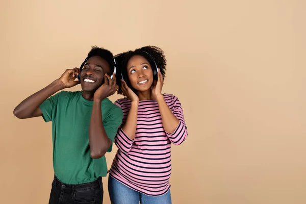 快乐的年轻黑人男人和女人在无线耳机大肚子听音乐 享受空闲时间 孤立在米色背景下 工作室 父母与家庭 关系与怀孕 — 图库照片