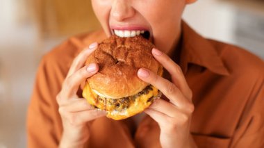Yakın çekimde, tanınmayan bir kadının lezzetli hamburgerleri ısırması ve yemesi, fast food 'un tadını çıkarması, öğle yemeğinde hile yapması, kırpılmış, panorama