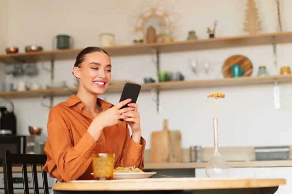 Vidám Kaukázusi Hölgy Asztalnál Konyhában Használja Mobiltelefon Étkezés Közben Böngészés — Stock Fotó