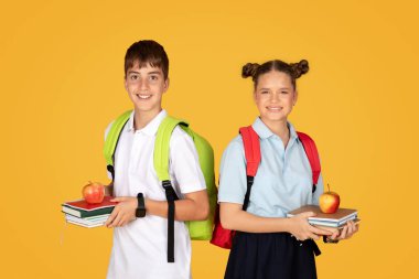 Portakal rengi stüdyo arka planında kitap ve elma bulunan mutlu beyaz kız ve erkek öğrenciler. Öğle yemeği molası ve dinlenme, birlikte eğitim, okulda eğitim, reklam ve teklif