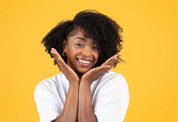 穿着白色T恤的积极的年轻黑人卷曲女士用手触摸着脸 享受着美感 被橙色背景隔离 工作室 生活方式 人类情感 广告和服务 — 图库照片