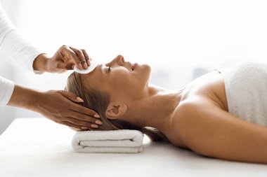 Kozmetik uzmanı, pamuk pedi ile güzel orta yaşlı bir kadının cildini temizliyor, modern spa salonlarında rahatça yüz bakımı yapıyor, güzellik salonunda sağlık günü düzenliyor.