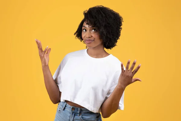 白いTシャツの混乱した黒いカーリーの若い女性は オレンジ色の背景 スタジオで孤立した 側面に腕を広げます 知らない 人間の感情 広告と提供 — ストック写真