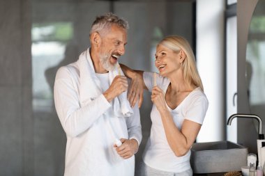 Mutlu eşlerin tuvalette dişlerini fırçalarken eğlenmesi, diş fırçasıyla evde diş temizliği yapan mutlu, yaşlı bir çiftin portresi,