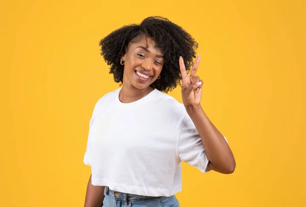 快乐的年轻黑人卷曲女士 身穿白色T恤 手握和平标志 与橙色背景隔离 工作室 生活方式 广告和服务 闲暇时间和乐趣 — 图库照片