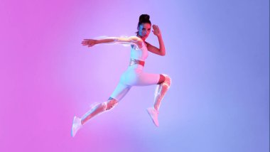 Atlayan Atletik Kadın, stüdyoda Pembe ve Mavi Neon geçmişine bakarak kamera karşısında poz veriyor. Tam Uzunluk, Boşluklu Panorama. Spor ve Teknoloji Konsepti. Spor Teknolojisi