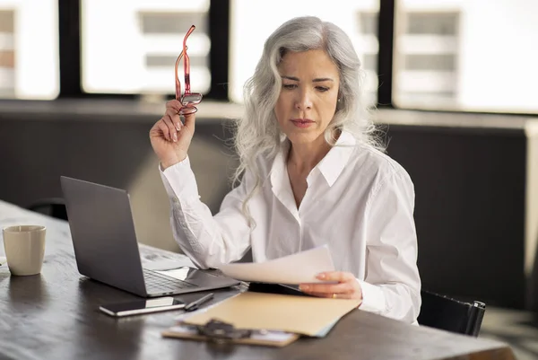 stock image Businesswoman Doing Paperwork Writing Reports, Looking At Papers And Documents Holding Glasses, Sitting At Table With Laptop In Modern Office. Manager Lady Reading Proposals And Resume At Workplace