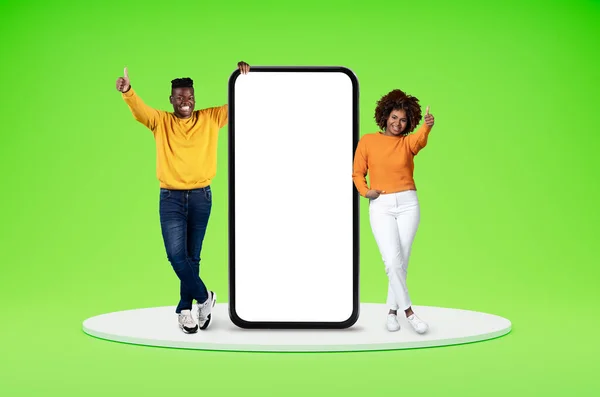 与移动应用程序的概念约会 快乐的千年黑人男女休闲地站在平台上 拿着大手机 白色的空白屏幕 展示大拇指 复制空间 与绿色背景隔离 — 图库照片