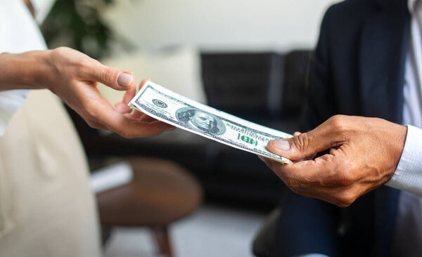 Caucasian old businessman in suit gives money dollars cash to woman hand in office interior, close up, cropped. Finance work and modern business, salary and profit, credit
