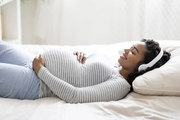 Ευτυχισμένη Μαύρη Έγκυος Γυναίκα Ξαπλωμένη Στο Κρεβάτι Ακούγοντας Μουσική Και — Φωτογραφία Αρχείου