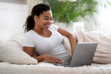 Çevrimiçi İş. Evde yatarken dizüstü bilgisayar kullanan gülümseyen siyah kadın, mutlu Afrikalı Amerikalı kadın klavyede yazı yazıyor, uzaktan kumandalı işten ve serbest çalışmadan keyif alıyor, boşluğu kopyalıyor.